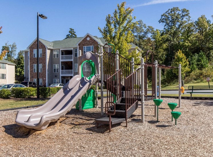 Wooden Playground with Green Accents on Mulch with Building Exterior and Treeline in the Background